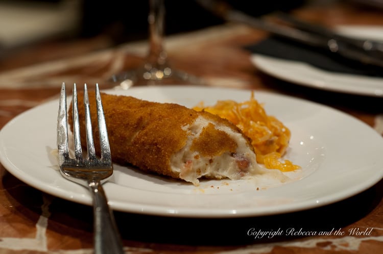 A close-up of a plate with a single croquette cut open, revealing a creamy filling, next to a fork on a table. Tapas are one of the highlights of Southern Spain.