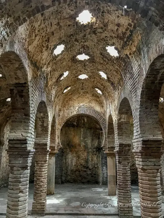 The interior of an ancient brick structure with a series of arches supporting a roof, with light filtering through the openings. This is the inside of the old Arab Baths in Ronda, Spain.