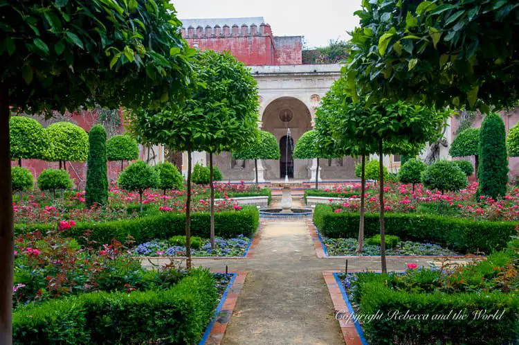 A meticulously maintained garden featuring symmetrical plantings, pathways, and a central fountain, reminiscent of traditional Andalusian courtyards. The gardens of the Casa de Pilatos in Seville, Spain, are beautiful - and it's one of the least touristy places to visit in Seville.