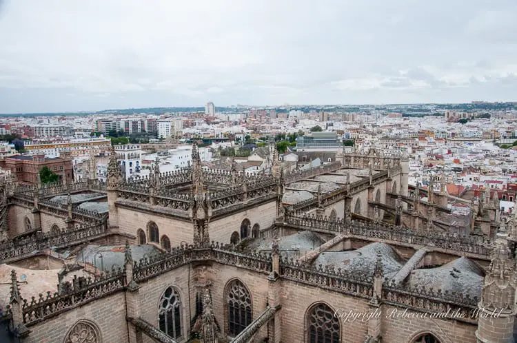 An aerial view of Seville, showcasing the expansive Gothic architecture of a cathedral with intricate spires and a sprawling urban landscape in the background. Climb La Giralda in Seville, Spain, for great views of the city.