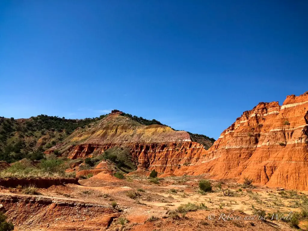Striking red and yellow stratified cliffs under a bright blue sky at Palo Duro Canyon, showcasing the park's unique geological features. One of the coolest things to do in Amarillo is visit nearby Palo Duro Canyon, the second largest canyon in the United States.