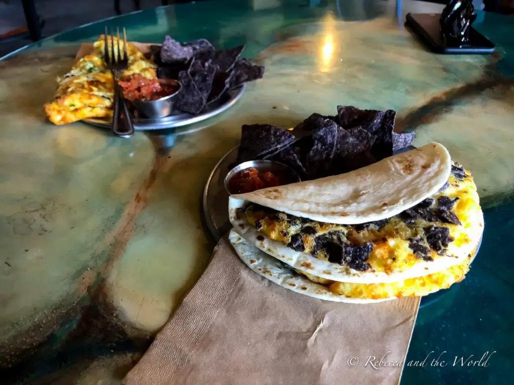 A plate of migas with melted cheese and black beans, served with a side of blue corn tortilla chips and salsa, on a metal table. The Sunday Brunch at 806 Lounge in Amarillo, Texas, is one of the best examples of delicious Amarillo food.