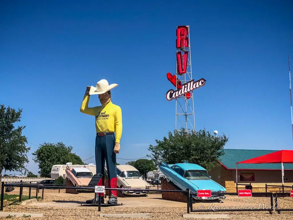 A large statue of a cowboy tipping his hat, with vintage cars and the Cadillac RV park sign in the background, under a bright blue Texas sky. A visit to Amarillo is a great way to see a different side to Texas.