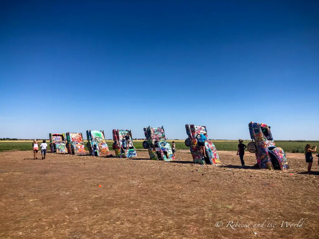 Colorful graffiti-covered cars planted upright in a field, known as Cadillac Ranch, with visitors walking around and taking photos. Cadillac Ranch in Amarillo, Texas, is one of the best places to visit in Amarillo.