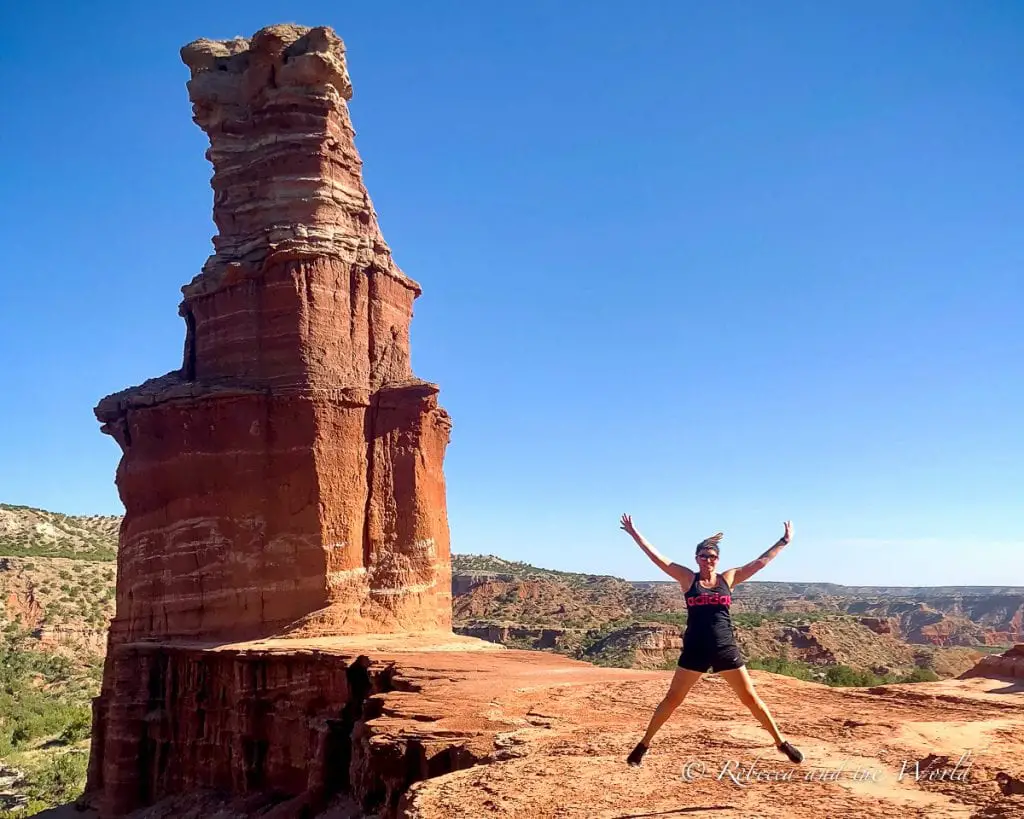 A person - the author of this article - joyfully jumping with arms raised in front of the Lighthouse rock formation in Palo Duro Canyon State Park, under a clear blue sky. One of the coolest things to do in Amarillo is visit nearby Palo Duro Canyon, the second largest canyon in the United States.