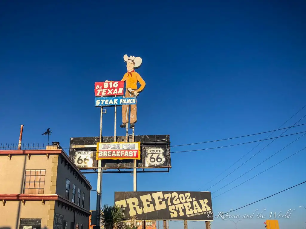 The iconic sign of The Big Texan Steak Ranch in Amarillo, featuring a large cowboy figure and Route 66 signage, against a clear blue sky. Many people visit Amarillo to attempt the 72 oz steak challenge!