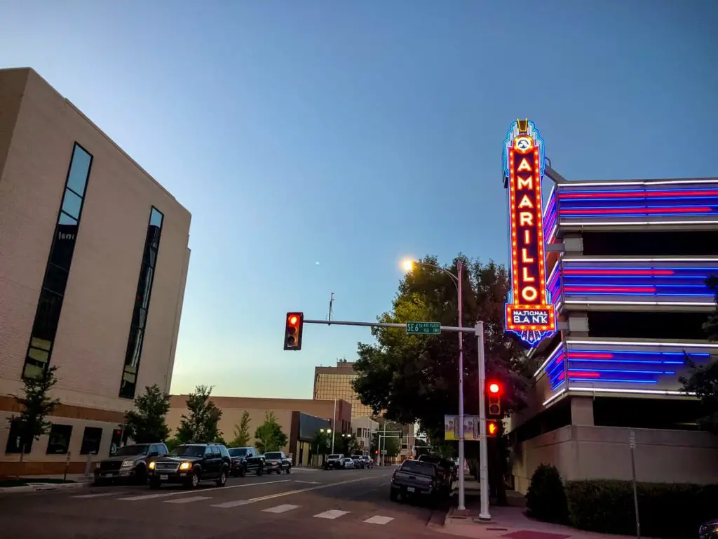 Neon-lit Amarillo National Bank sign against a dusky sky at twilight, with a traffic light showing red and cars waiting at an intersection.