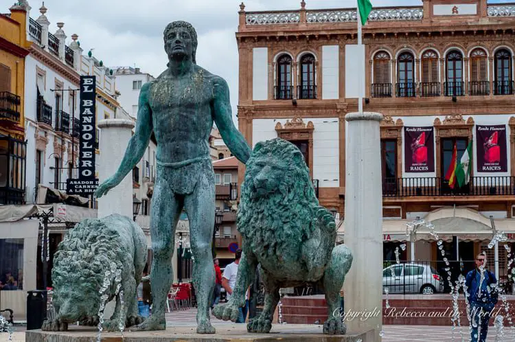 A bronze statue of a bullfighter accompanied by two bulls, located in a bustling square in Ronda, capturing the cultural significance of bullfighting in the town's history.