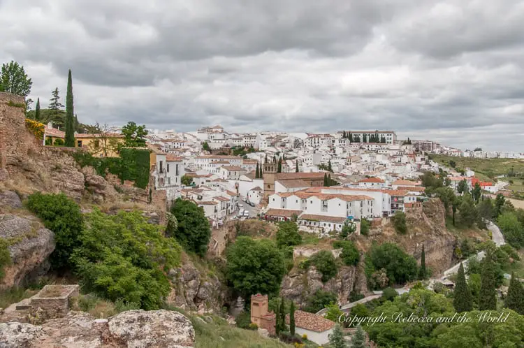 A panoramic view of Ronda, showcasing its white-washed buildings densely packed together, perched on the edge of a cliff, illustrating the town's dramatic setting in the mountainous terrain of Spain.