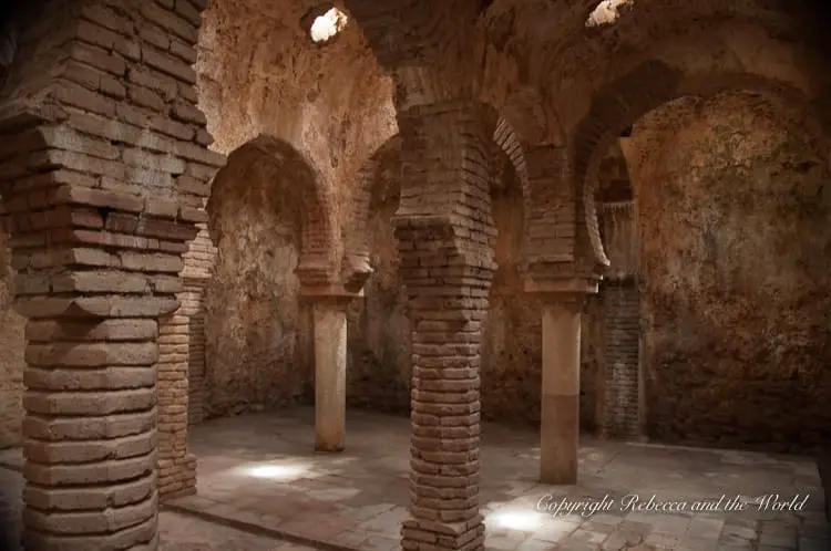 The Arab Baths in Ronda, featuring well-preserved brickwork arches and columns, with shafts of light filtering through the star-shaped openings in the ceiling, evoking a sense of historical serenity.