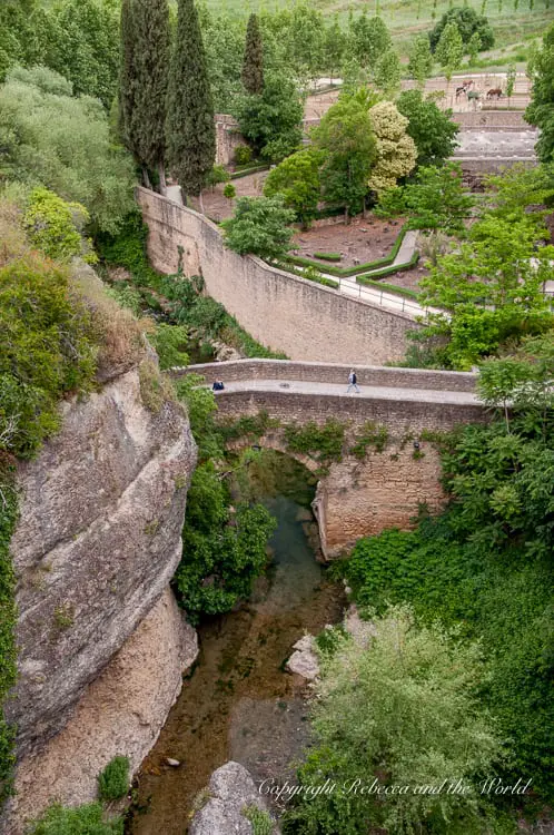 A view from above of a stone bridge crossing over a verdant gorge in Ronda, surrounded by trees and footpaths, inviting exploration of the town's natural beauty.