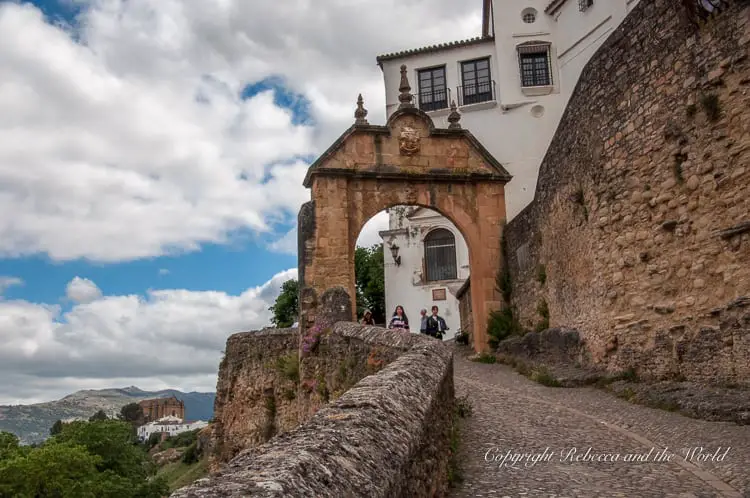 An ancient archway in Ronda, framed by a white building and a clear view of the landscape beyond, representing the historic gateways that lead to beautiful vistas.