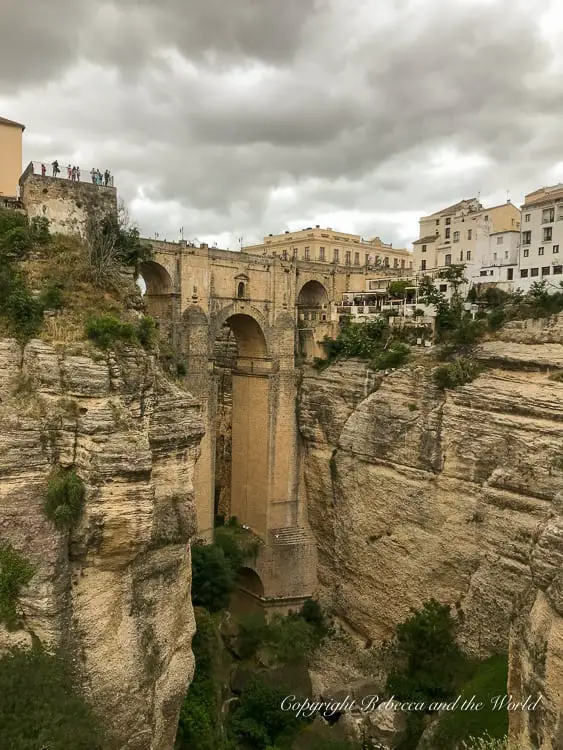 A distant view of the Puente Nuevo, Ronda's iconic bridge, towering over the El Tajo gorge, with buildings perched on the edge offering a dramatic architectural spectacle.