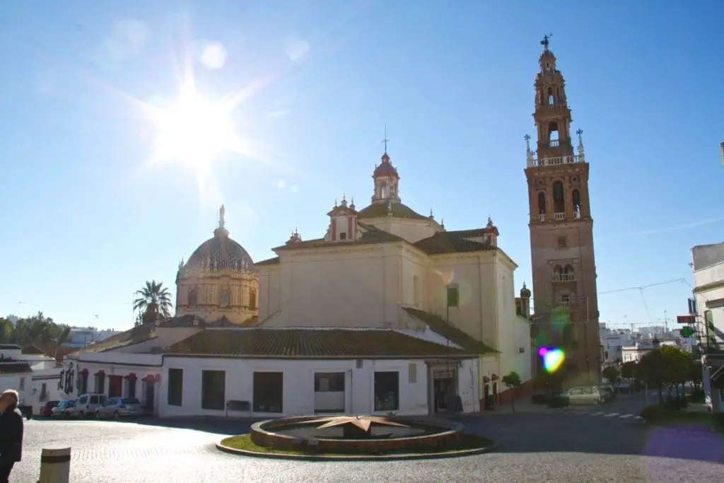 The sunburst behind the Church of the Annunciation in Carmona, with its detailed façade and tower bathed in sunlight, against a bright blue sky, reflecting the town’s tranquil ambiance.