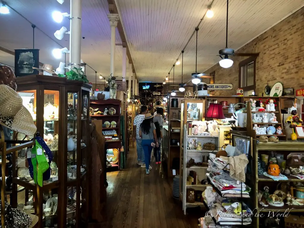 An antique shop interior with wooden floors, displaying various items like lamps, glassware, and memorabilia, with shoppers browsing the collection. There plenty of stores in the historic Gruene area to pick up a unique souvenir to remember your weekend in New Braunfels, Texas.