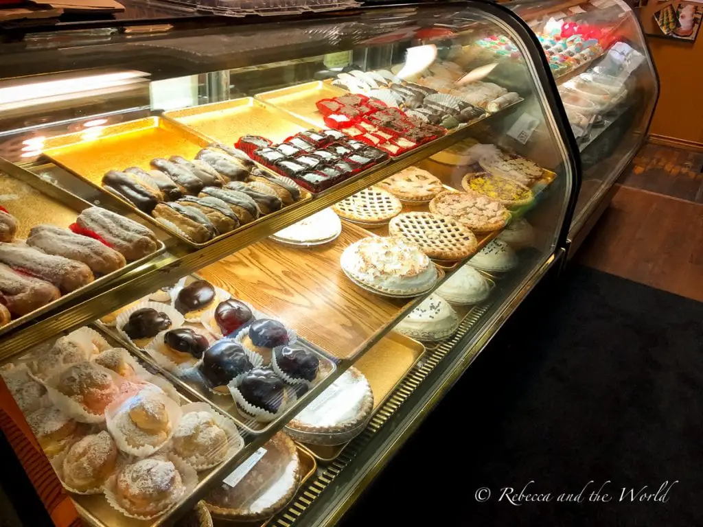 A bakery display case filled with assorted pastries including jelly-filled donuts, frosted cookies, and fruit tarts, all arranged neatly on trays. Every visit to New Braunfels should include a stop at Naegelin's Bakery for some treats.