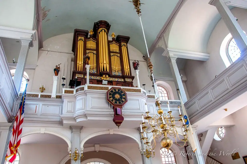 The interior of a historic church showing a large, ornate organ above a balcony, with elaborate gold decoration and a star-patterned clock. The Old North Church has played a key part in USA history.