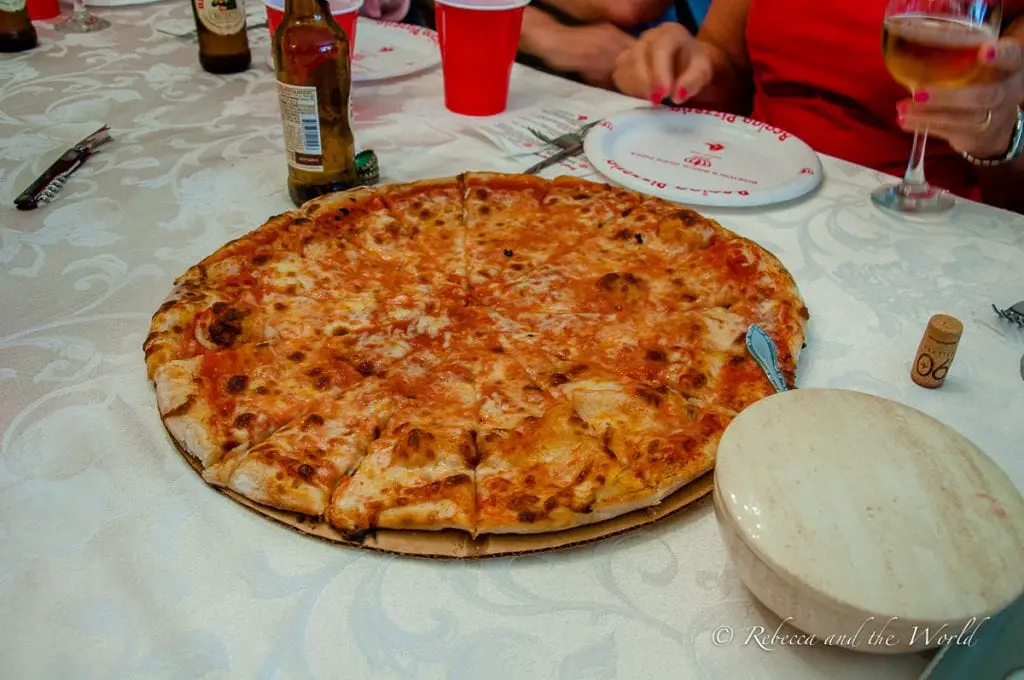 A large, round cheese pizza on a table, surrounded by glasses and condiments. Try Regina's famous pizza - the most famous pizza in Boston - on this food tour.