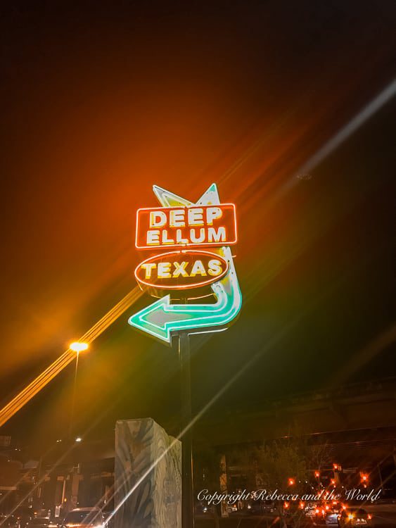 Neon sign of 'Deep Ellum Texas' with a stylized directional arrow, illuminated against a night sky. Deep Ellum is a must-visit neighbourhood on a weekend trip to Dallas, TX.