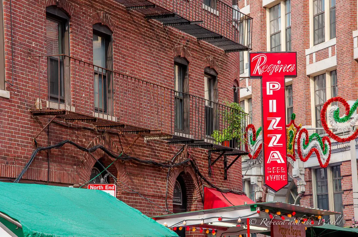 A vibrant street view in the North End featuring the Regina Pizzeria sign among traditional brick buildings adorned with festive decorations. Regina Pizzeria is one of the best pizza restaurants in Boston.