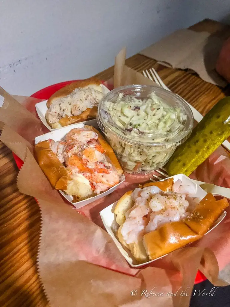 An assortment of seafood rolls, including lobster and shrimp, served with a side of coleslaw and a pickle on a paper-lined tray.