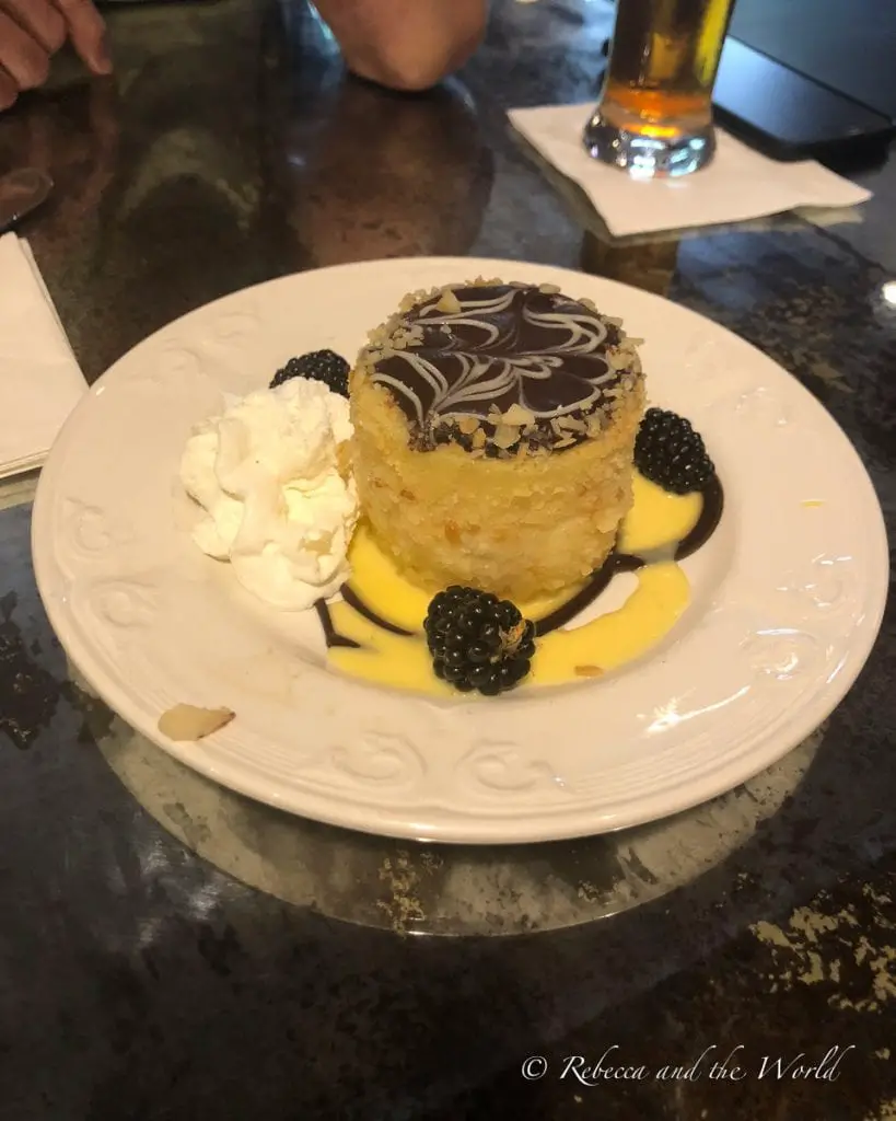 A plate with a round cake topped with a chocolate swirl design, surrounded by a pool of custard, accompanied by whipped cream and fresh blackberries. This is a Boston cream pie and it's well worth the calories!