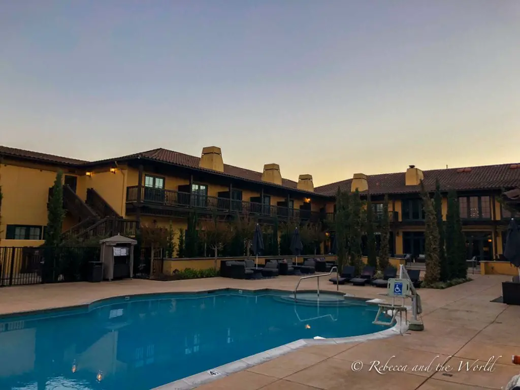 A tranquil hotel pool area at dusk with loungers and potted plants, and a three-story hotel building with balconies in the background under a fading sky. The Lodge at Sonoma Resort is one of the best hotels in Sonoma.