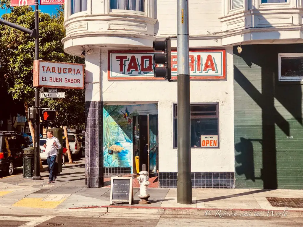 A street corner in San Francisco's Mission District, featuring "Taqueria El Buen Sabor." People are walking by and a street sign for 18th Street is visible. One of the best things to eat in San Francisco is a burrito from the Mission District.