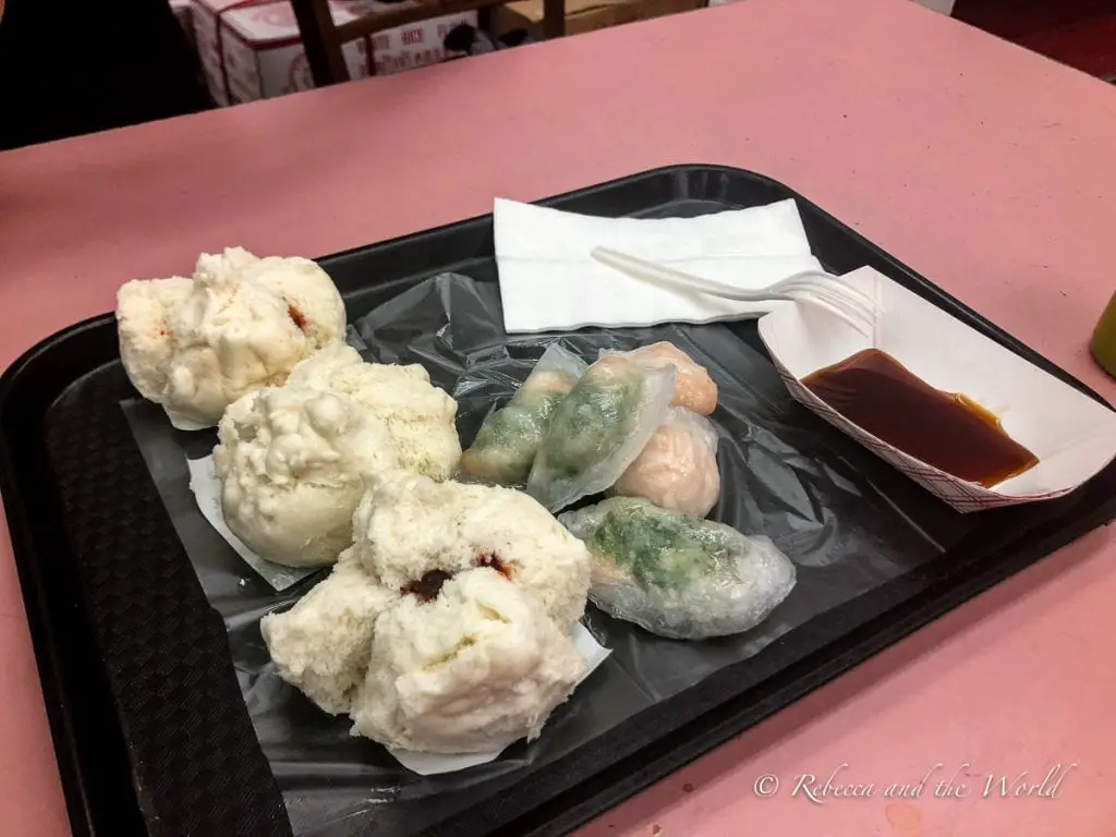 A tray with an assortment of steamed dumplings, alongside a small container of soy sauce, on a pink table. Wondering what to eat in San Francisco? Try the food at Delicious Dim Sum in Chinatown.