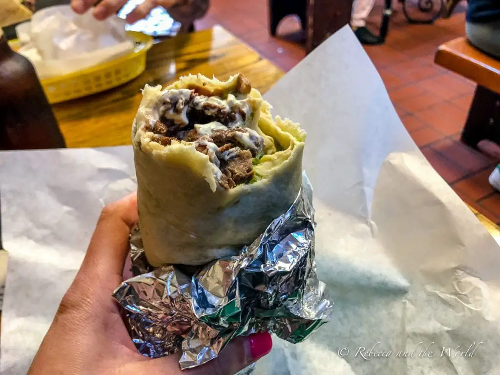 A close-up of a hand holding a foil-wrapped burrito, partially unwrapped to reveal a meat and cheese filling. The burrito at La Taqueria in San Francisco has been voted the best burrito in the world.