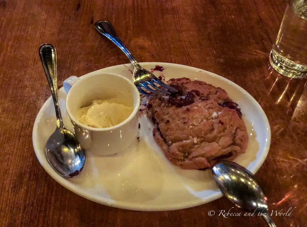 A freshly baked cookie with chunks of chocolate, served alongside a small cup of vanilla ice cream, on a white plate with two spoons, ready for sharing. Farm-to-table restaurant the girl and the fig in Sonoma is one of the best restaurants in Sonoma.