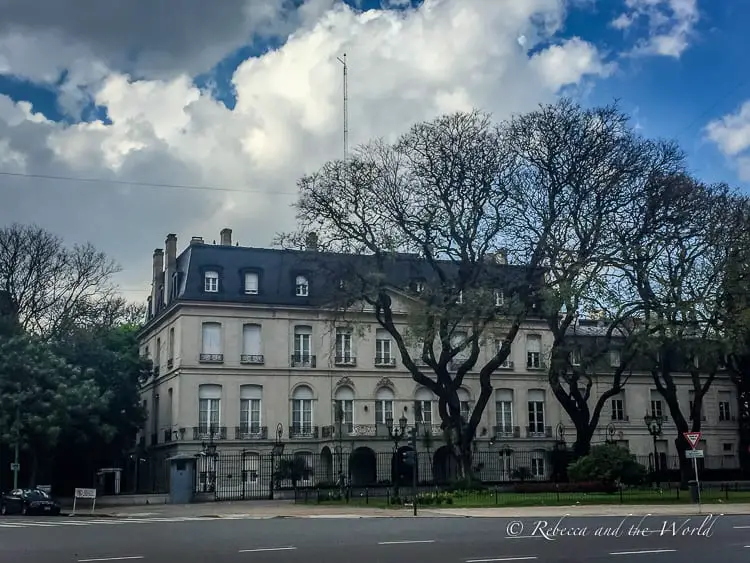 Buenos Aires is going to be your first stop with 2 weeks in Argentina. You'll see beautiful buildings like this one, a grand cream building with grey roof. Large trees - mostly leafless - are out the front and there's a blue sky with clouds.