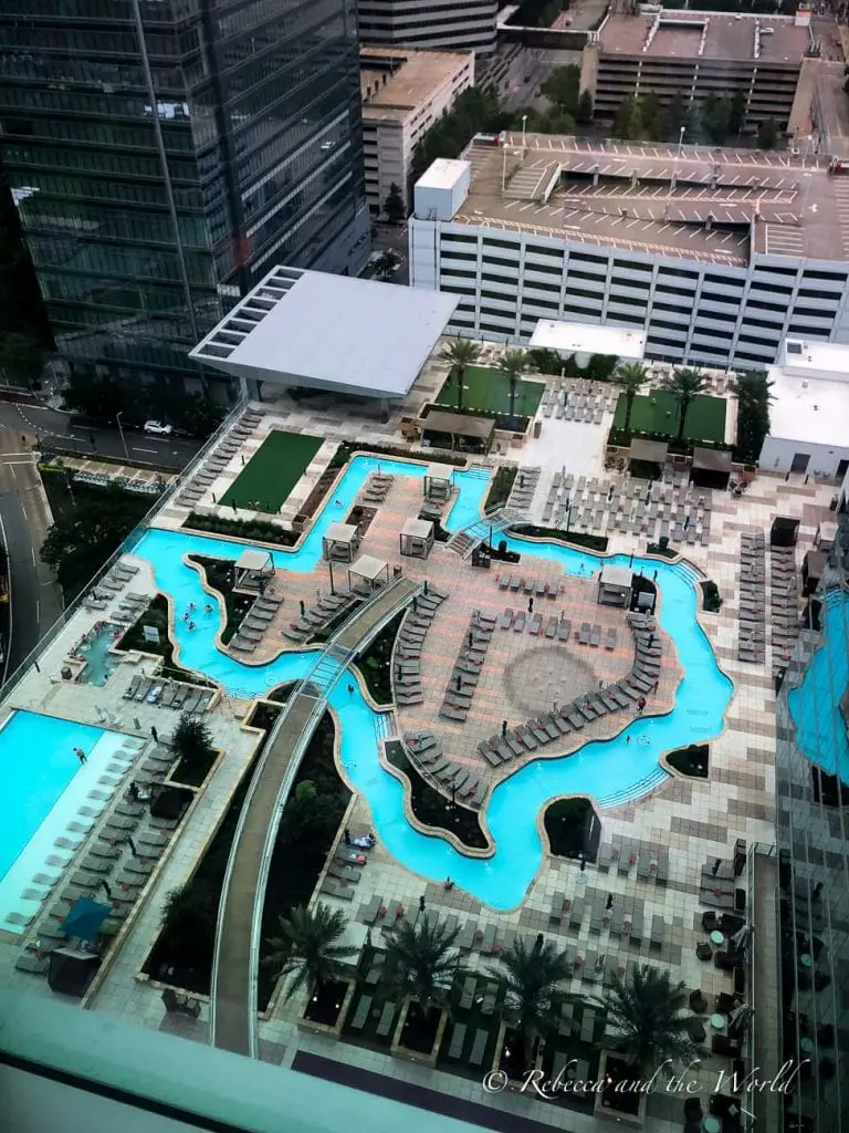 An aerial view of the Marriott Marquis Houston’s rooftop lazy river pool, which is shaped like the state of Texas. The pool area includes lounge chairs, greenery, and surrounding buildings. The Marriott Marquis Houston is a fun hotel to stay at.