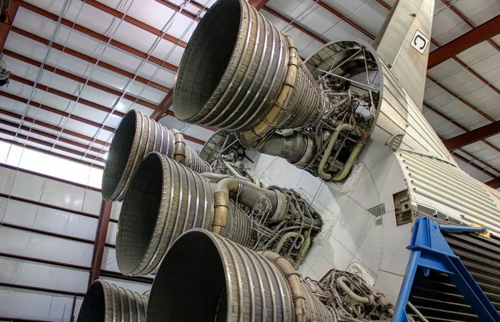 A close-up view of the massive engines of a Saturn V rocket, displayed indoors at the Space Center Houston. The engines are large and complex, with visible pipes and metal structures. Houston is home to the NASA Space Center.