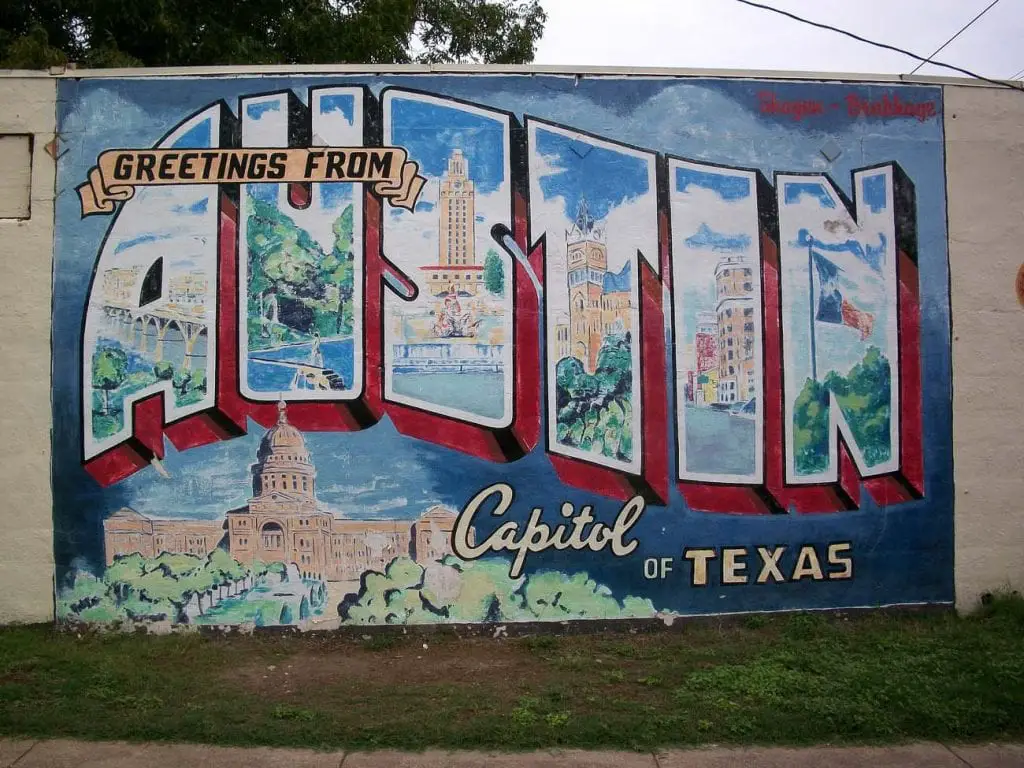 A vibrant mural in Austin that reads "Greetings from Austin, Capitol of Texas." The mural features images of local landmarks, including the Texas State Capitol and the UT Tower, painted in large, bold letters against a colorful background. Austin is one of the coolest places to visit in Texas.
