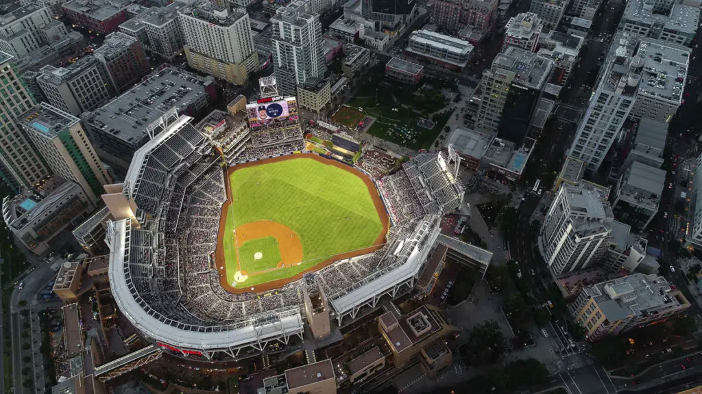 An aerial shot of a baseball stadium lit up for an evening game, surrounded by a dense urban environment at dusk. The Gaslamp neighbourhood is one of the best places to experience San Diego nightlife.