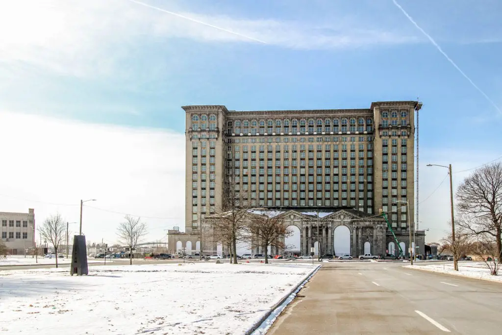 Exterior of the abandoned Michigan Central Station in Detroit, with snow on the ground and a clear blue sky above. Check out the city's architecture on your weekend in Detroit.