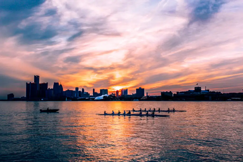 A crew team rowing in the Detroit River at sunset with the city skyline silhouetted in the background. Belle Isle is one of the most beautiful places in Detroit to catch the sunset.