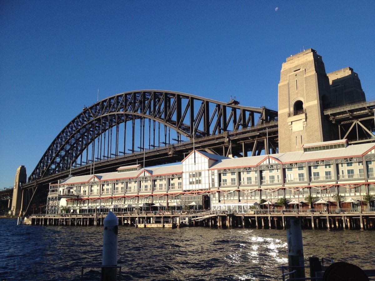 View of the Sydney Harbour Bridge, an iconic steel arch bridge with a backdrop of clear blue sky, alongside historic waterfront buildings at Dawes Point. The Sydney Harbour Bridge is one of the most popular things to see in Sydney, Australia.