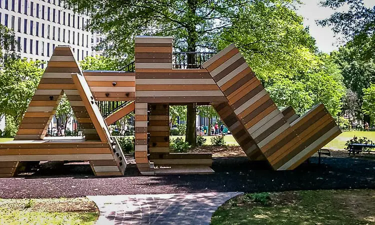 A unique, large wooden play structure in a park, resembling the letters 'ATL' that form interconnected slides and platforms.