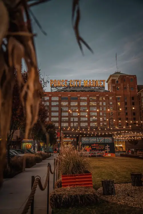 Nighttime view of Ponce City Market in Atlanta Georgia, a large brick building with lit signage, bustling with activity against a dusky sky.