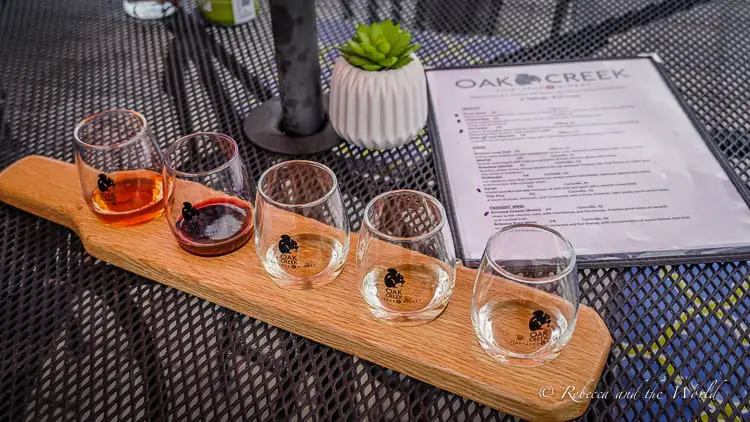 A wooden flight board with six glasses of wine, ranging in color, accompanied by a tasting menu on a table with a mesh pattern, reflecting a wine tasting experience in Sedona.