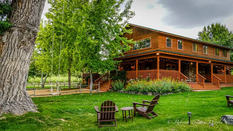 A cozy wooden lodge surrounded by a fence, green lawn, and mature trees, offering a sense of the rustic wineries in Sedona.