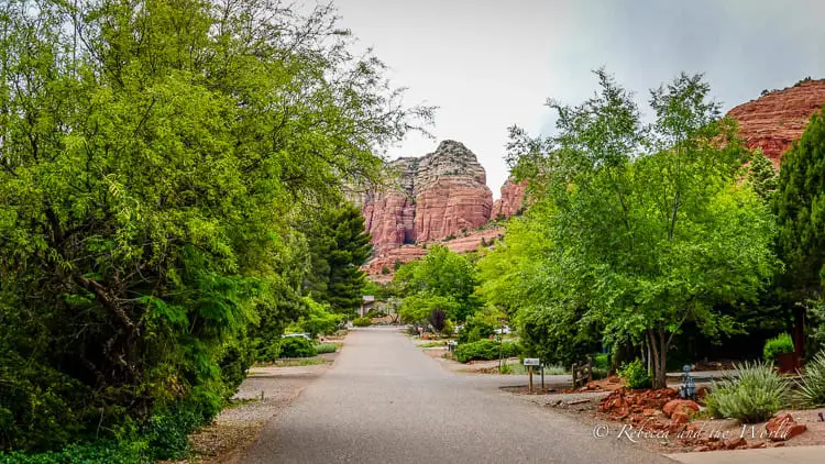 A serene residential street in Sedona, flanked by vibrant green trees and with a striking red rock backdrop, showcasing the town's peaceful living environment.