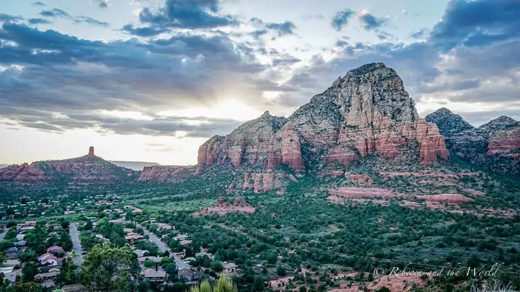 A dramatic evening sky over the layered red rock mountains of Sedona, with the last rays of sunlight illuminating the rock formations, and the town nestled in the valley below.