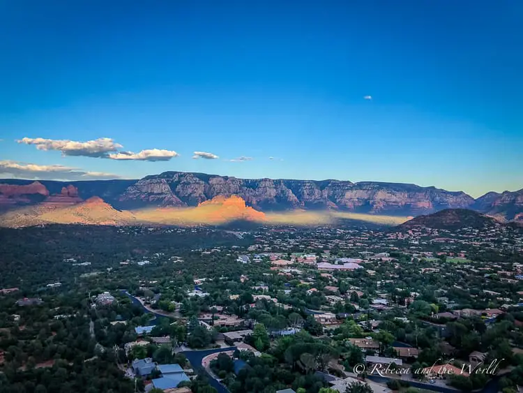 An aerial view of Sedona at dusk, capturing the sprawling town with its lights beginning to twinkle and the surrounding mesas and buttes shaded by the setting sun.