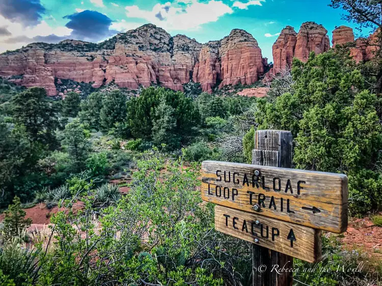 A wooden trail sign reading "Sugarloaf Loop Trail" with an arrow pointing right, set against a backdrop of vibrant red rock formations and green foliage. This is one of the easiest but best hikes in Sedona, AZ.