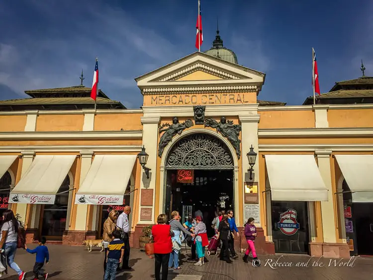 The entrance to "Mercado Central" in Santiago Chile with people entering and exiting the building, under a sign with the market's name and the Chilean flag above.