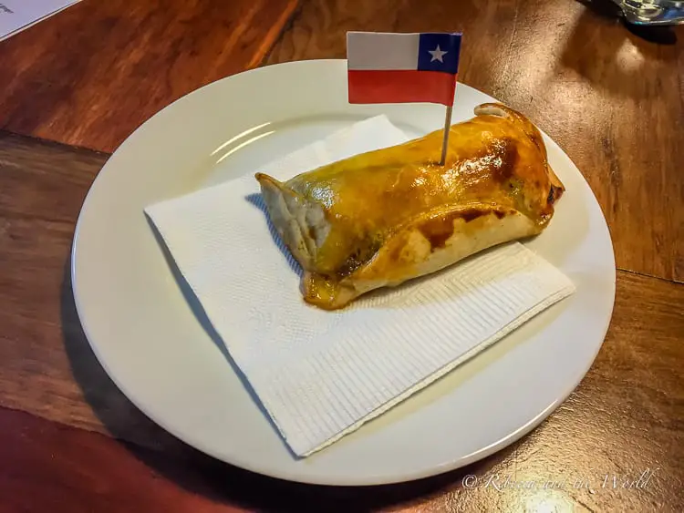A plate with an empanada topped with a small Chilean flag on a toothpick.