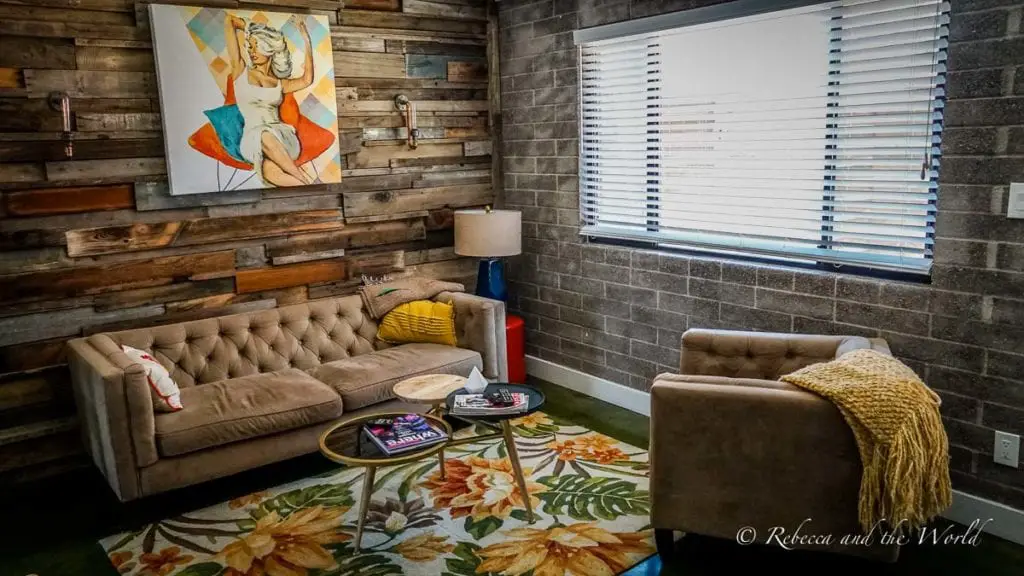 A cozy room with a tufted sofa, armchairs, a colorful rug, and a painting of a woman in a swimsuit on a wooden wall. We booked a great Airbnb in Phoenix when we visited.